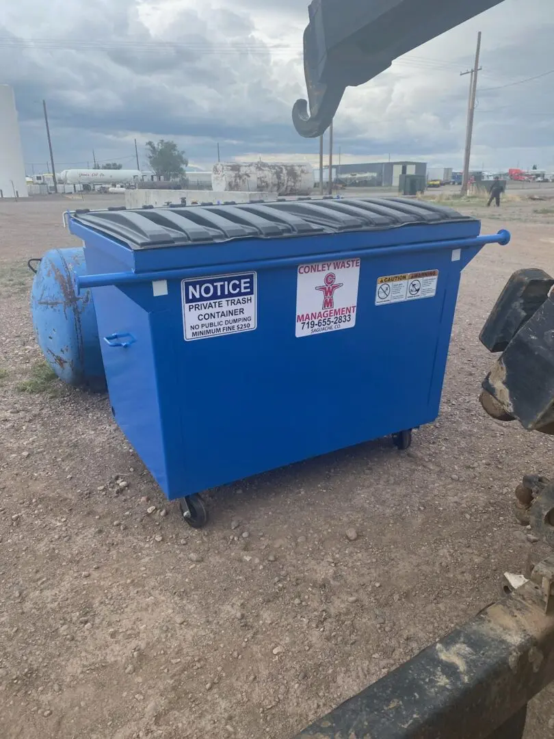 A dumpster with signs on it sitting in the dirt.