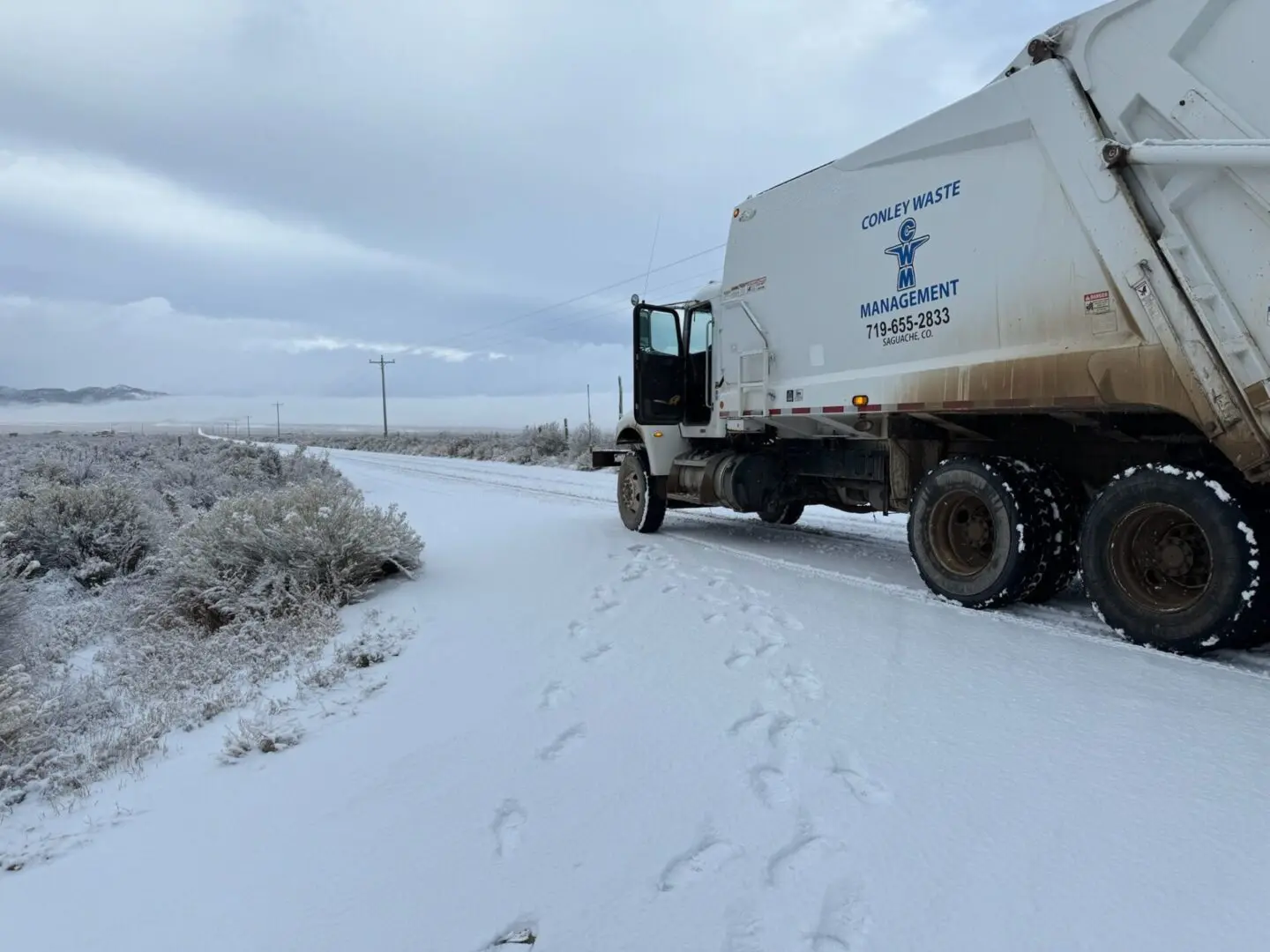 A garbage truck is parked in the snow.