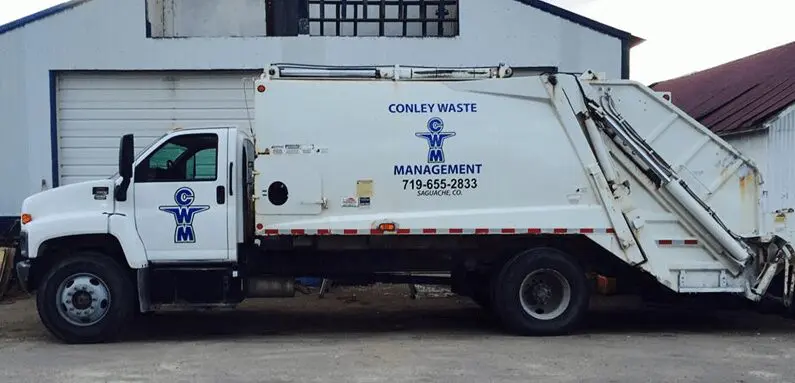 A white garbage truck parked in front of a building.